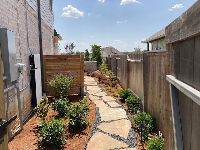 Stone pathway winds through a narrow yard with landscaping and a wooden fence.