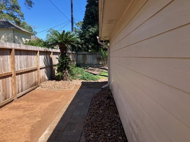 Side yard with wooden fence, brick path, tan siding, and small plants.