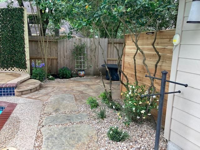 Backyard with a stone path, wooden fence, small plants, and a hot tub.