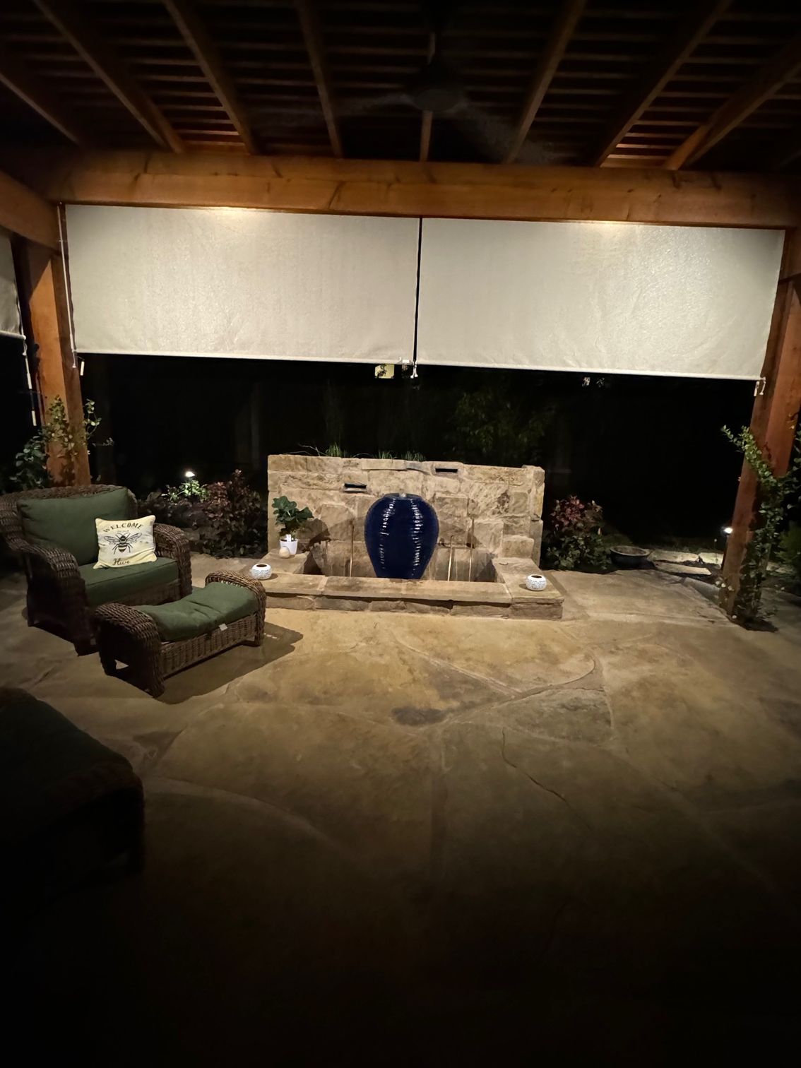 Outdoor patio at night with a stone fireplace, seating, and overhead screens.