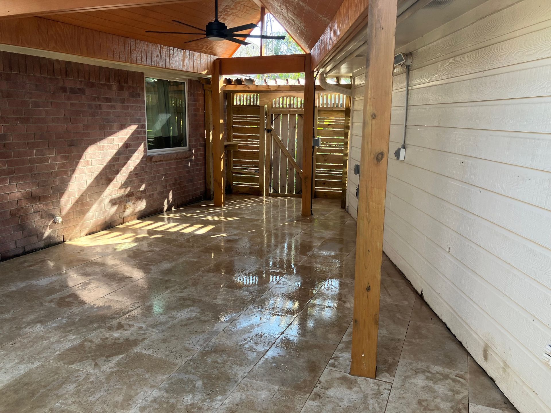 Covered outdoor patio with wet, polished concrete floor, wooden posts, and a rustic wooden shower enclosure.