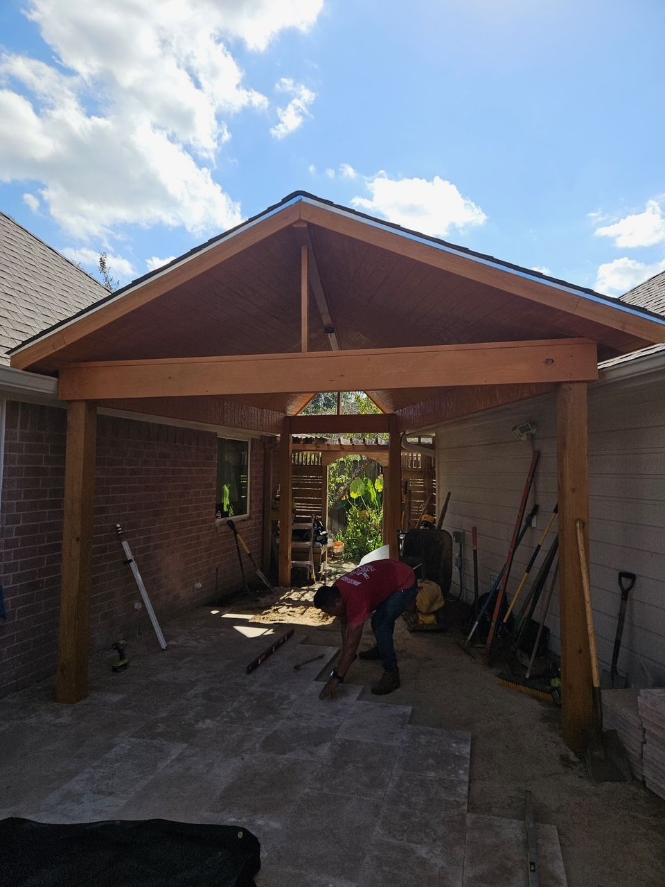 A man is working on a wooden patio cover attached to a brick and a white-painted wall.