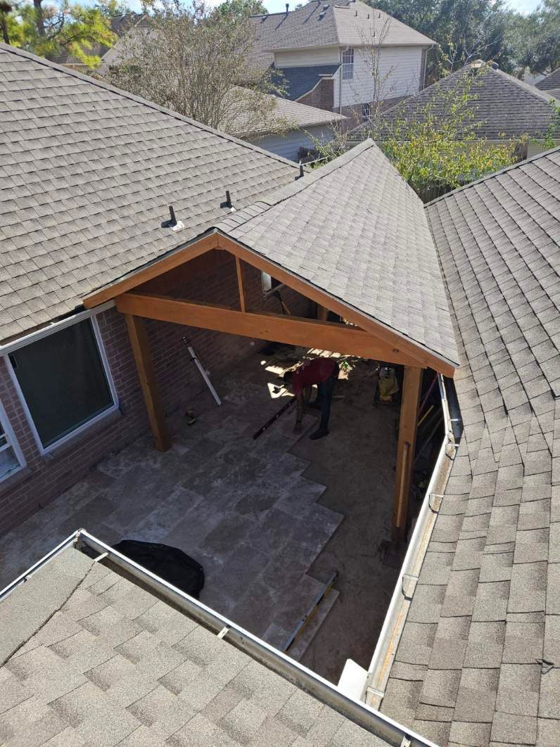 Overhead view of a patio with a wooden pergola. Brown roof tiles and a person working inside the pergola.