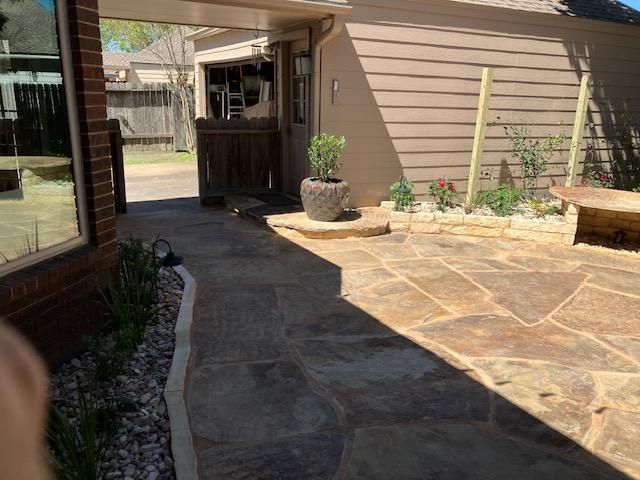 Stone patio with a pathway leading to a door and a potted plant. Sunny day.