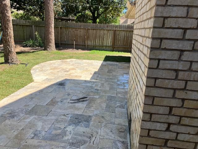 Backyard patio with stone pavers, grass, a wooden fence, and a brick wall.