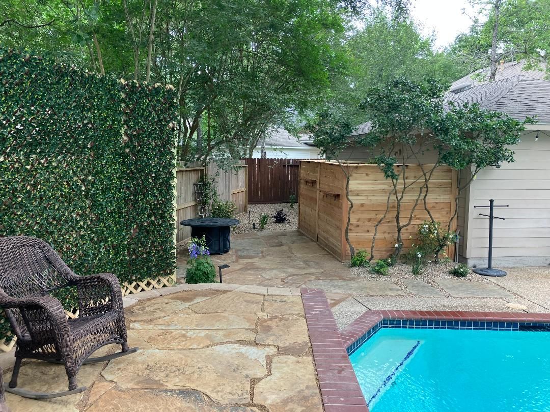 Backyard with pool, stone patio, wooden fence, climbing plants, and a wicker chair.