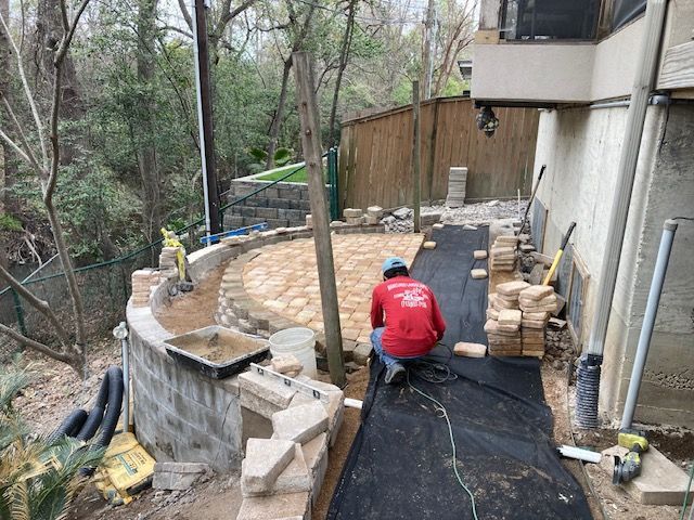 Construction worker laying pavers in a backyard with a curved brick wall.