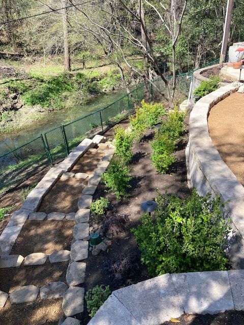 Stone steps and landscaping lead to a river, with a green fence and retaining walls.