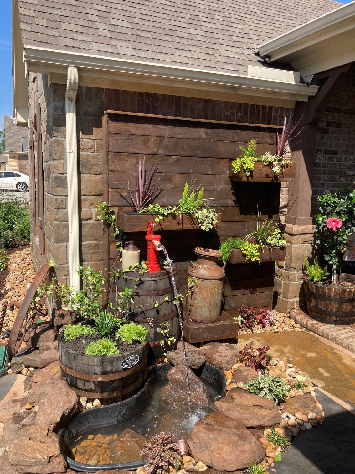 Water feature with a wooden wall, plants, and a small pond in front of a house.