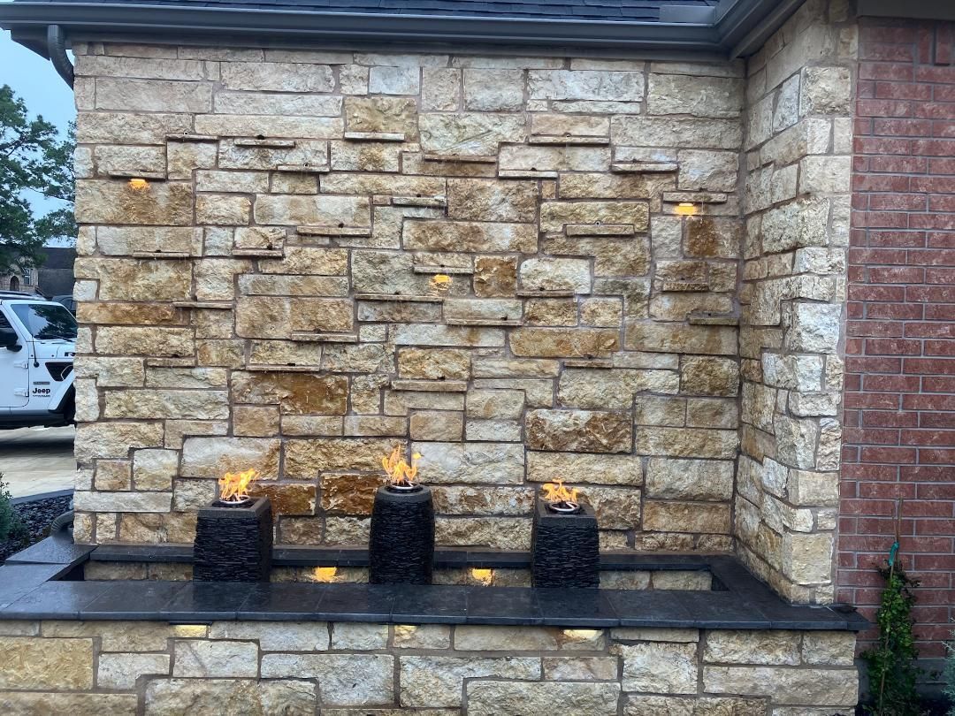 Stone water feature with flames and lights against a stone wall.
