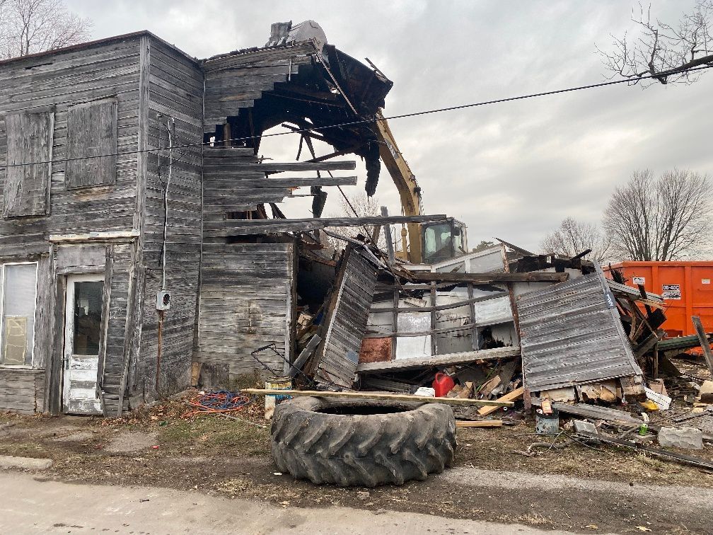 Demolition of a weathered wooden building; excavator visible.