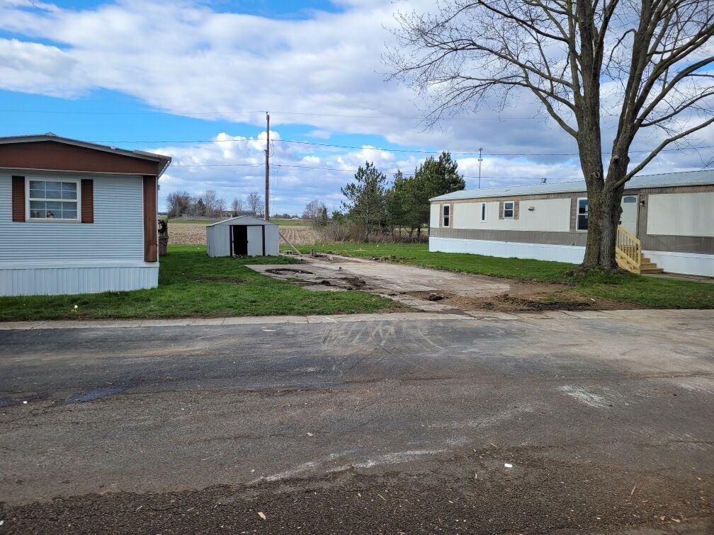 Mobile homes on a road, partly cloudy sky, grass, and a small shed in the background.