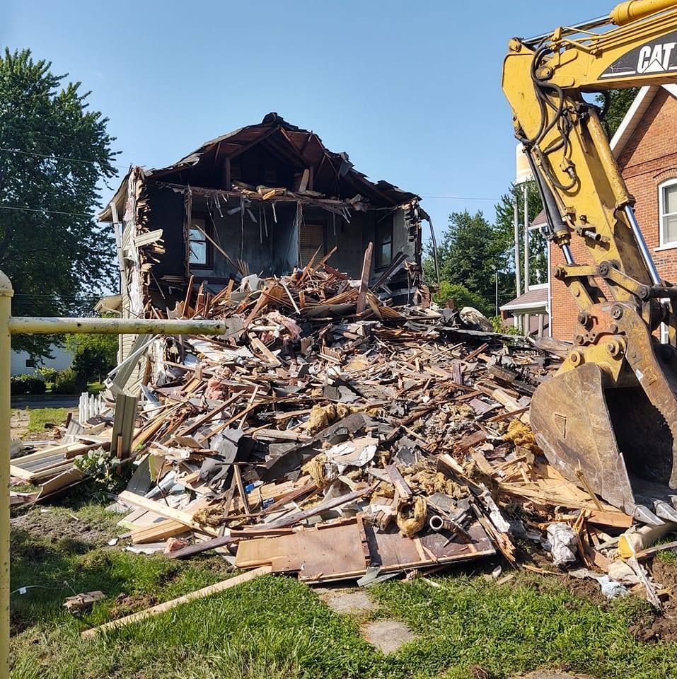 Demolished house with an excavator removing debris; sunny day.