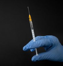 A person wearing blue gloves is holding a syringe.
