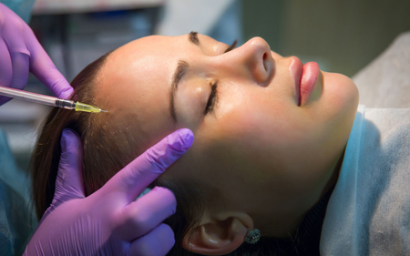 A woman is getting a botox injection in her forehead.