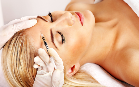 A woman is getting a botox injection in her forehead.