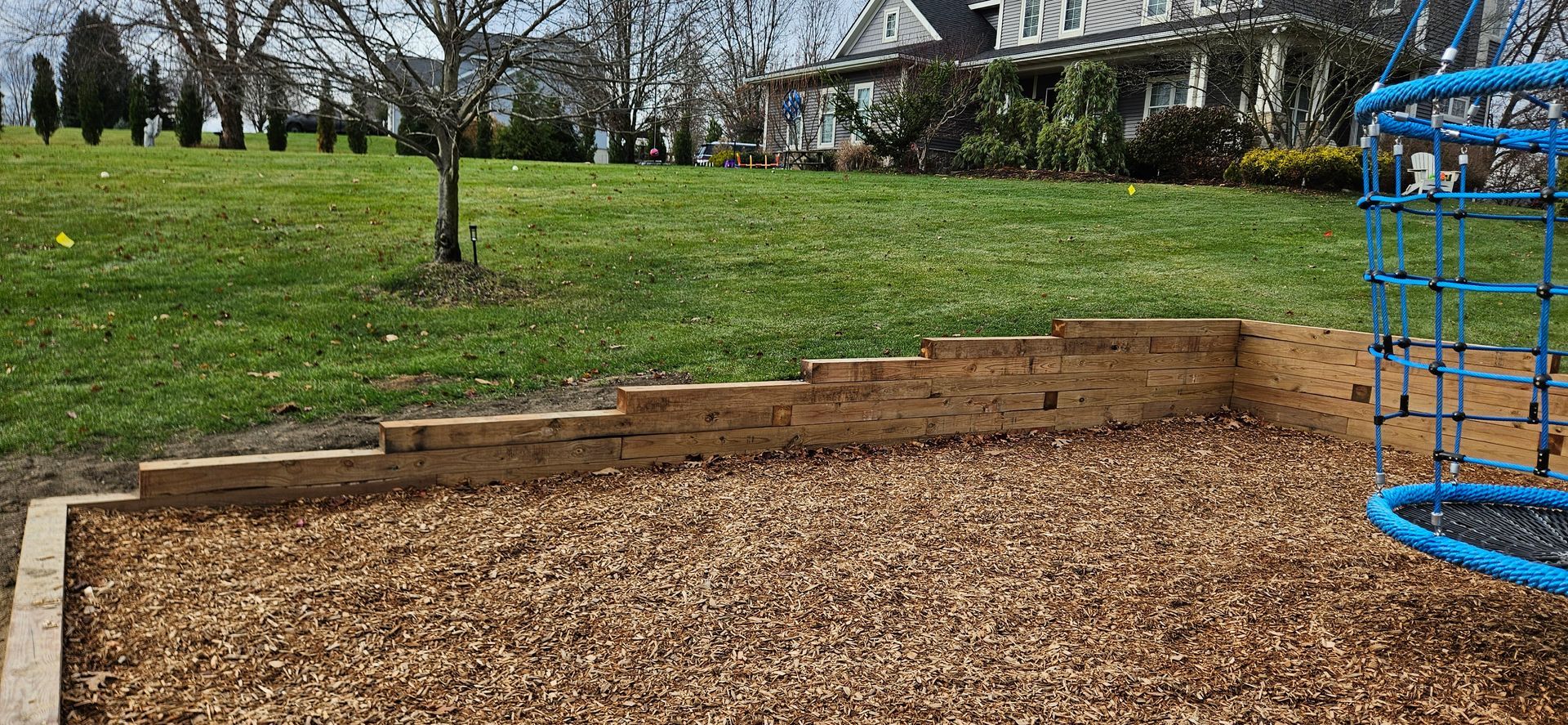 A playground with a blue ladder and a brick wall in a park.