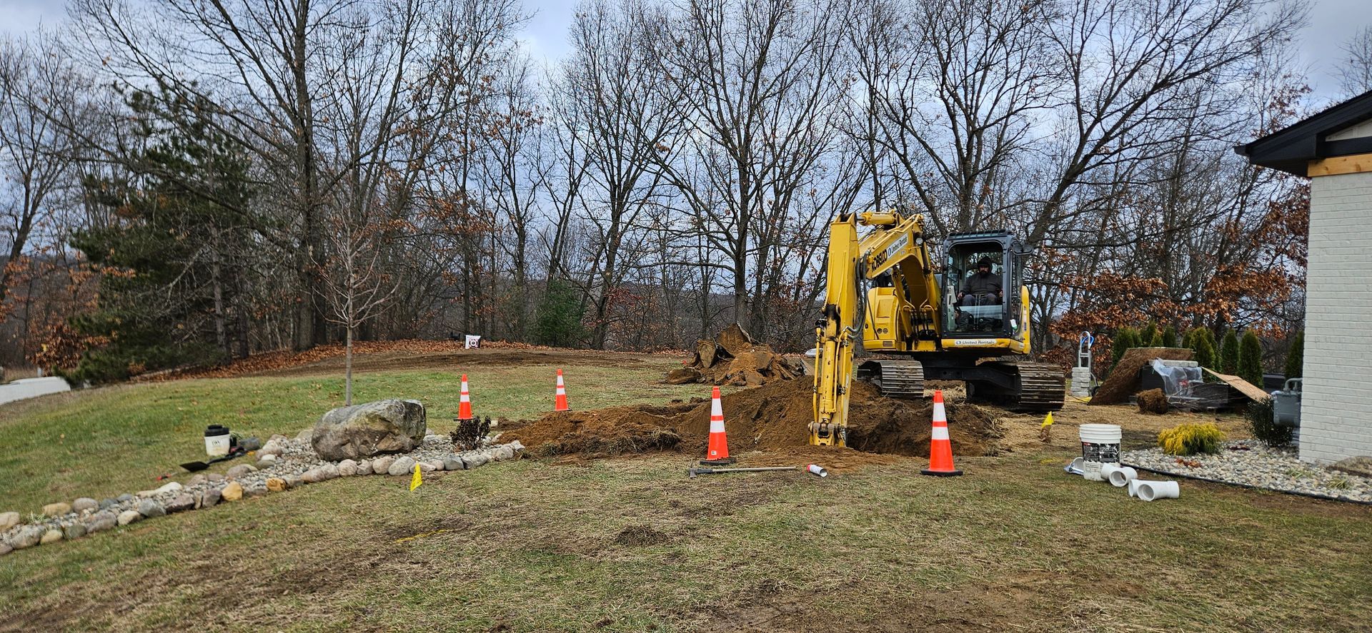A yellow excavator is digging a hole in a yard.