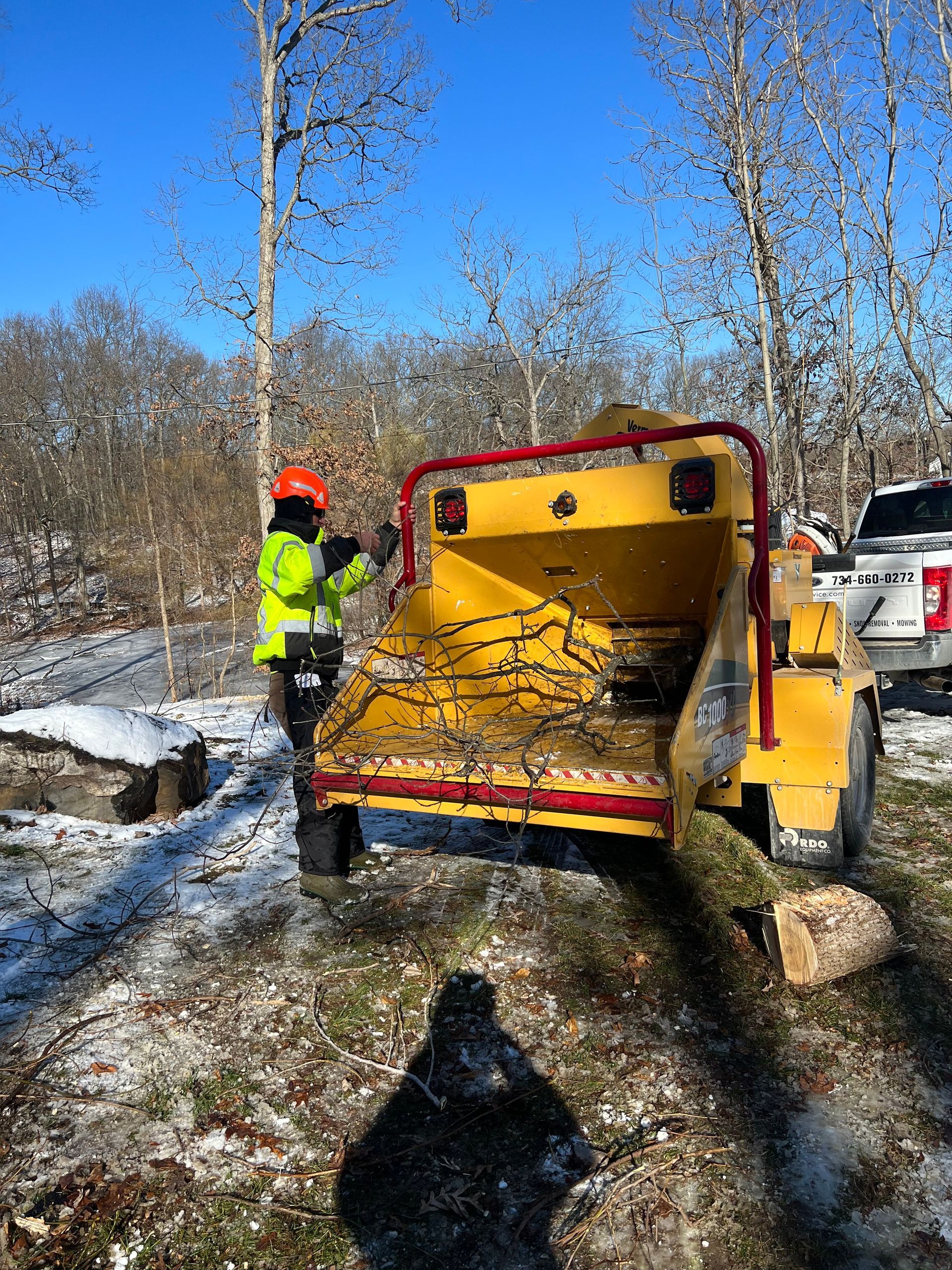 A man is standing next to a tree chipper in the snow.