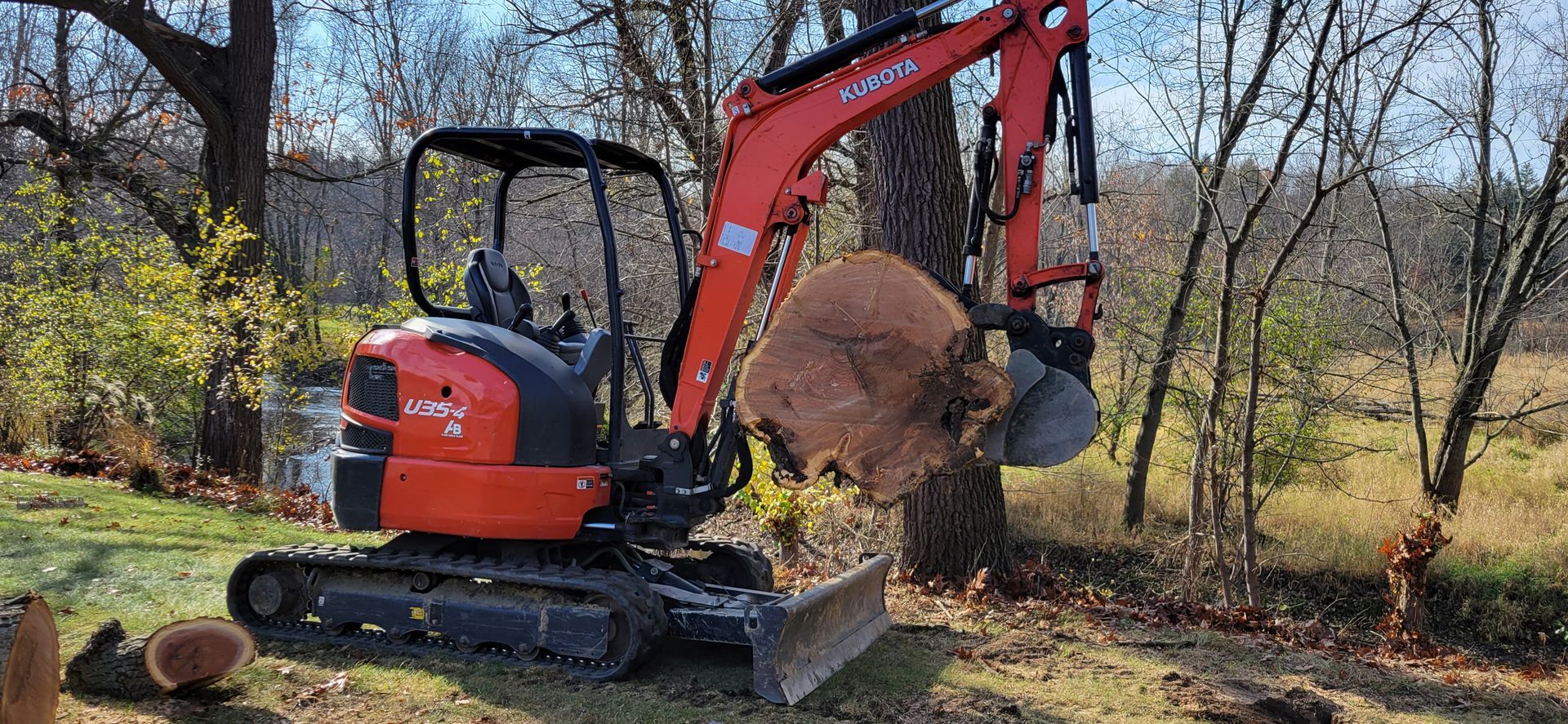 A small excavator is carrying a large log in its bucket.