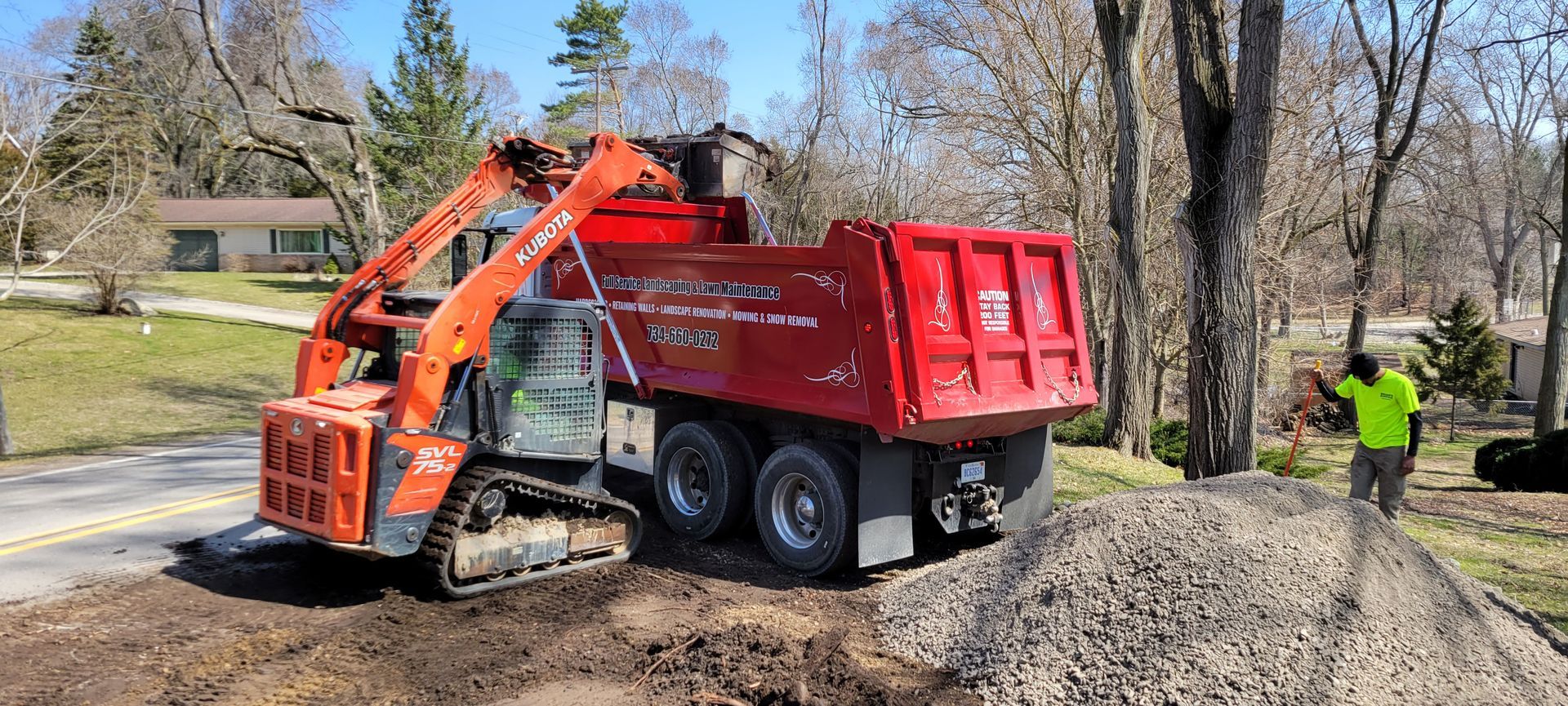 A red dump truck with a crane attached to it is driving down a dirt road.