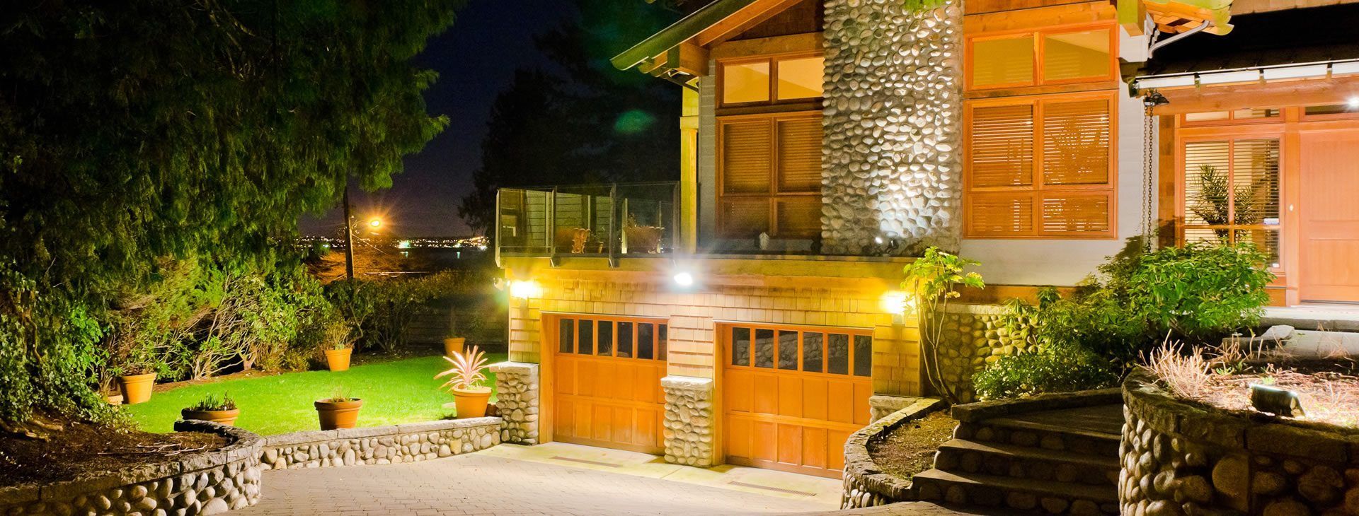 A large house with a wooden garage door is lit up at night.