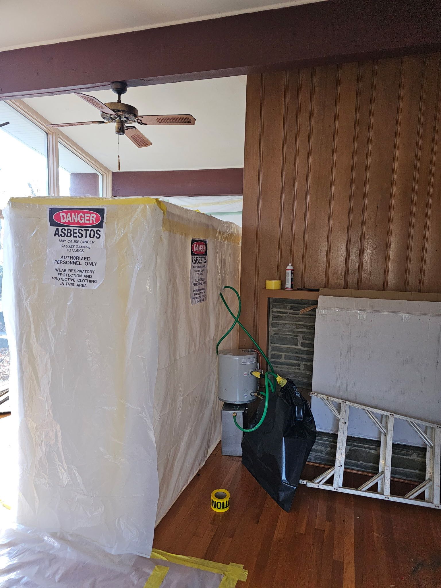 Large, wrapped structure inside a home, possibly for remediation. Brown wood paneling on wall, open doorway.
