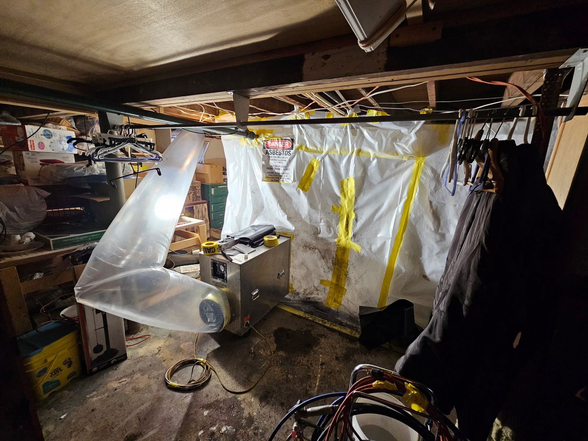 A cluttered workshop with a contained workspace constructed of plastic sheeting and a ventilation tube attached to equipment.