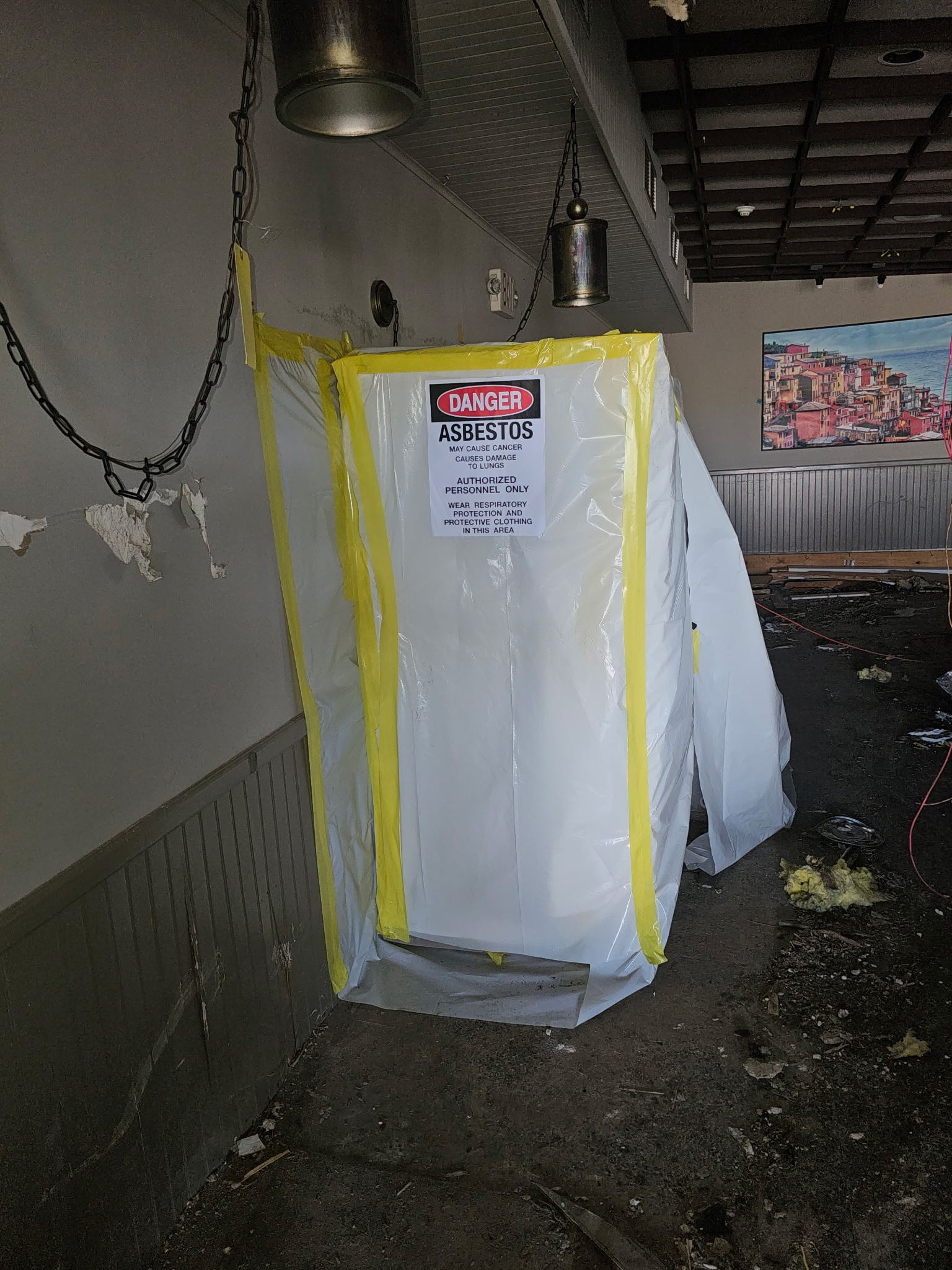 A plastic debris containment bag hangs near a ceiling. The bag has yellow tape and a hazard sign.