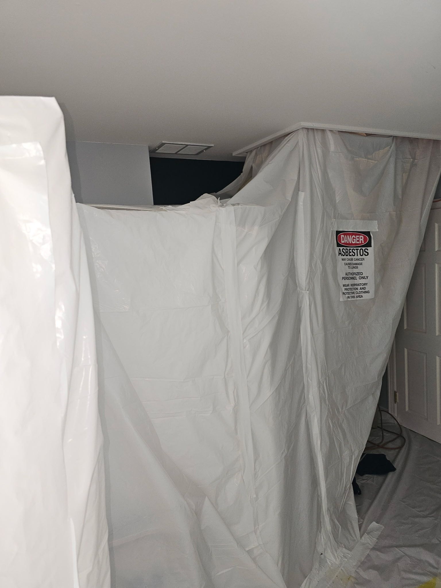 White plastic sheeting seals off a room, possibly for construction or remediation, with a warning label attached.