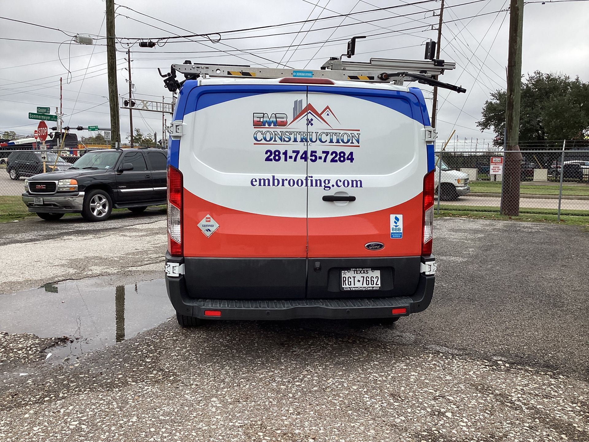 Back of a construction van with company logo parked on gravel.