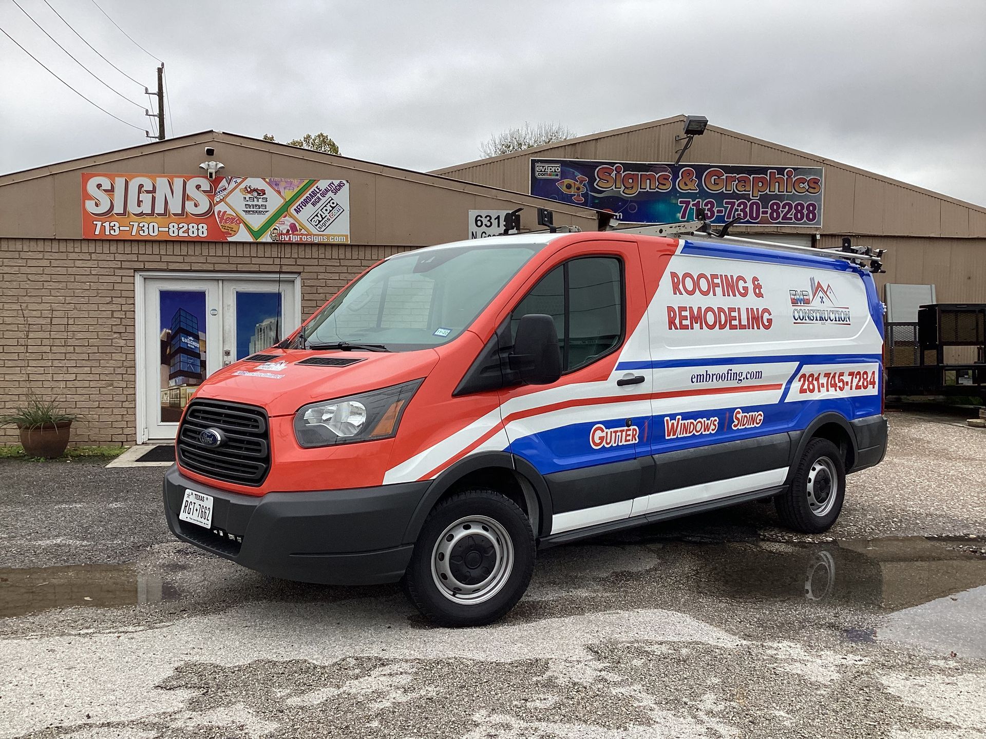 A red, white, and blue Roofing's Remodeling van parked outside a brick building with 