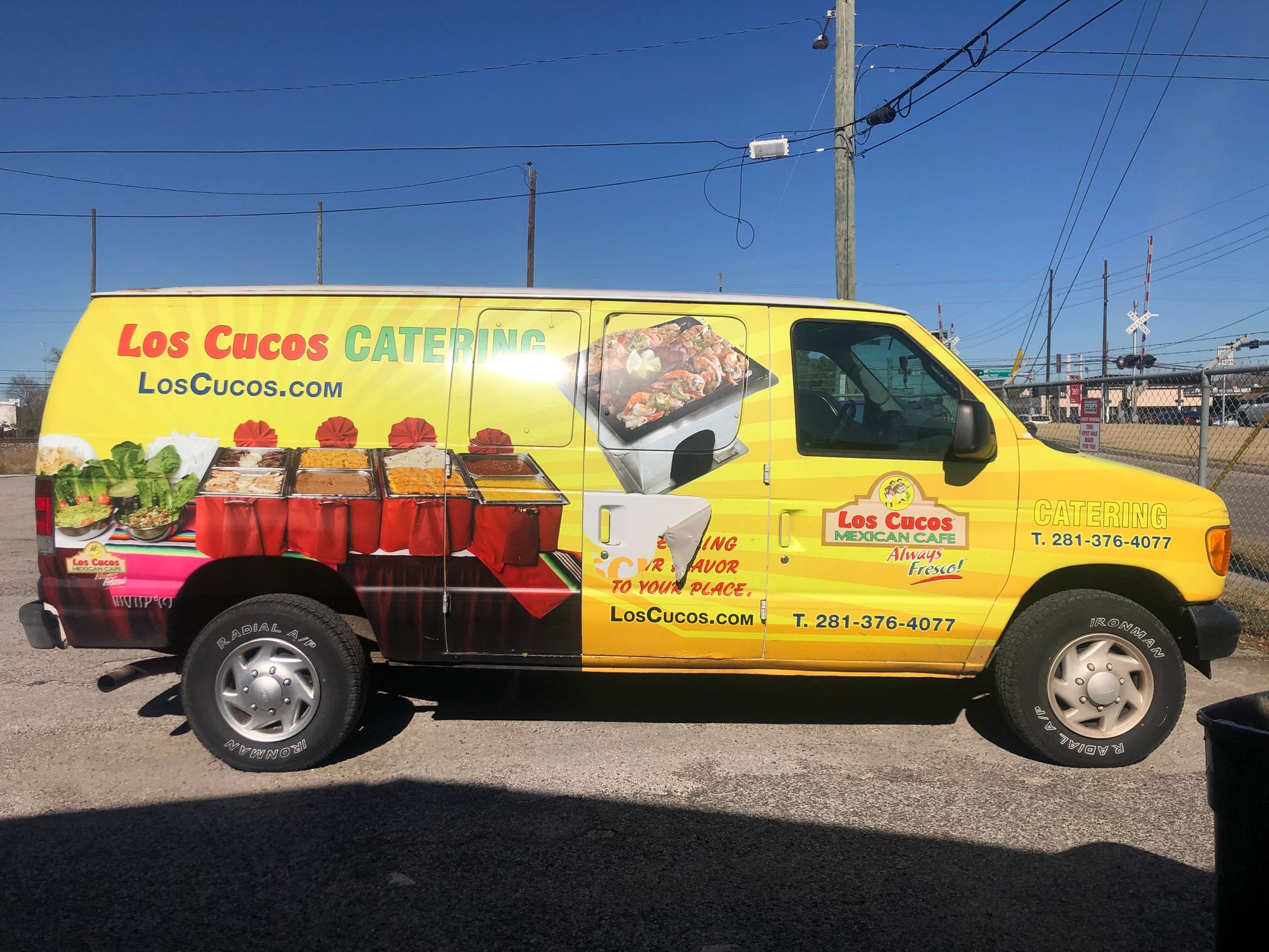 Yellow Los Cocos Catering van parked on a street with advertisements for food.