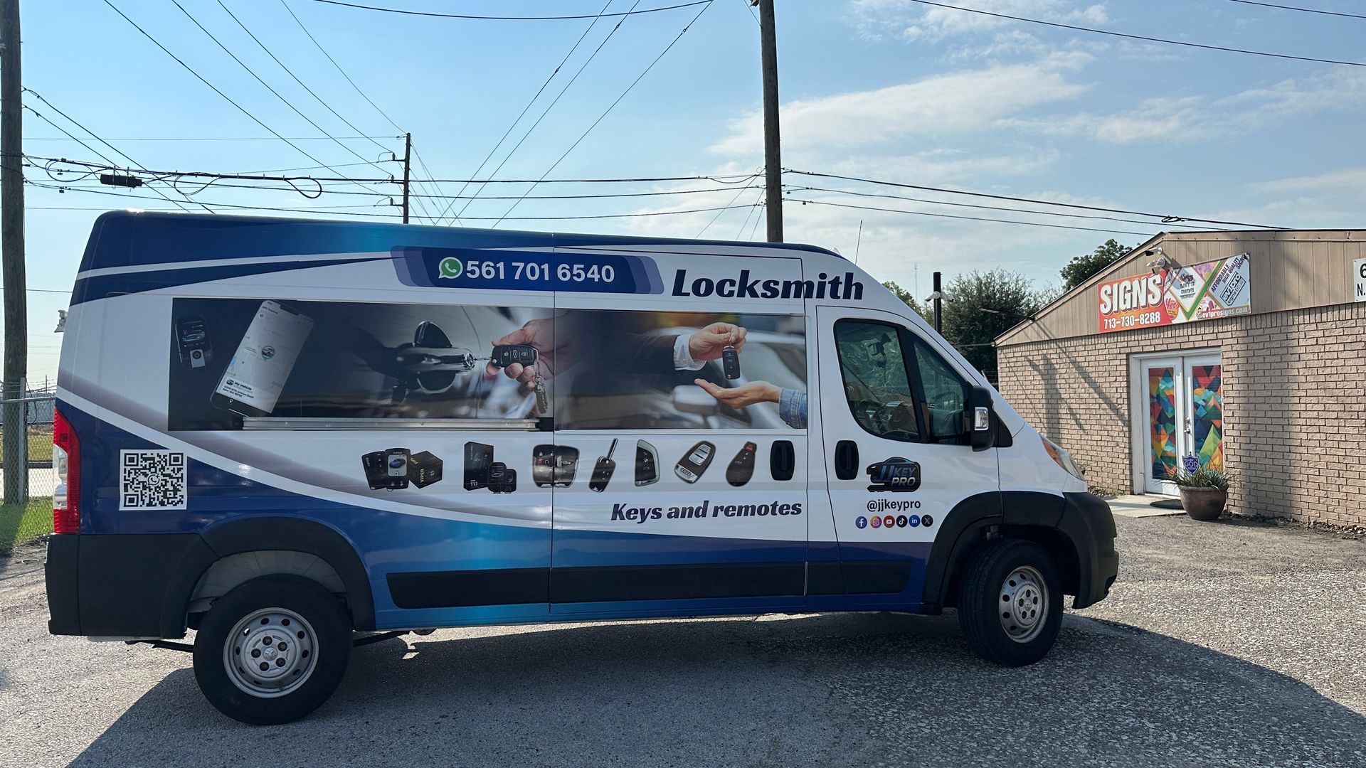 Locksmith van with blue and white wrap, parked in front of a small building under a blue sky.
