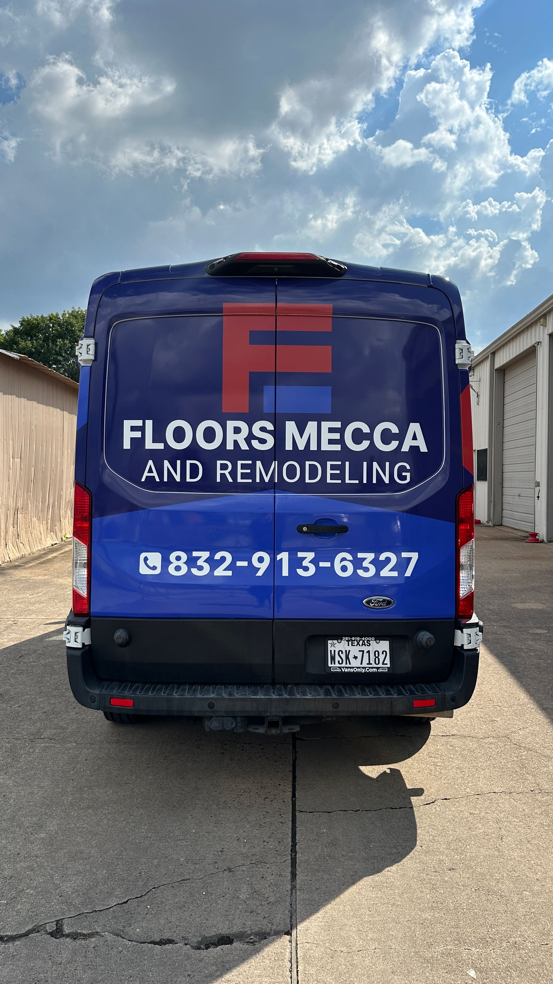 Blue van with Floors Mecca logo and phone number, parked outside buildings.