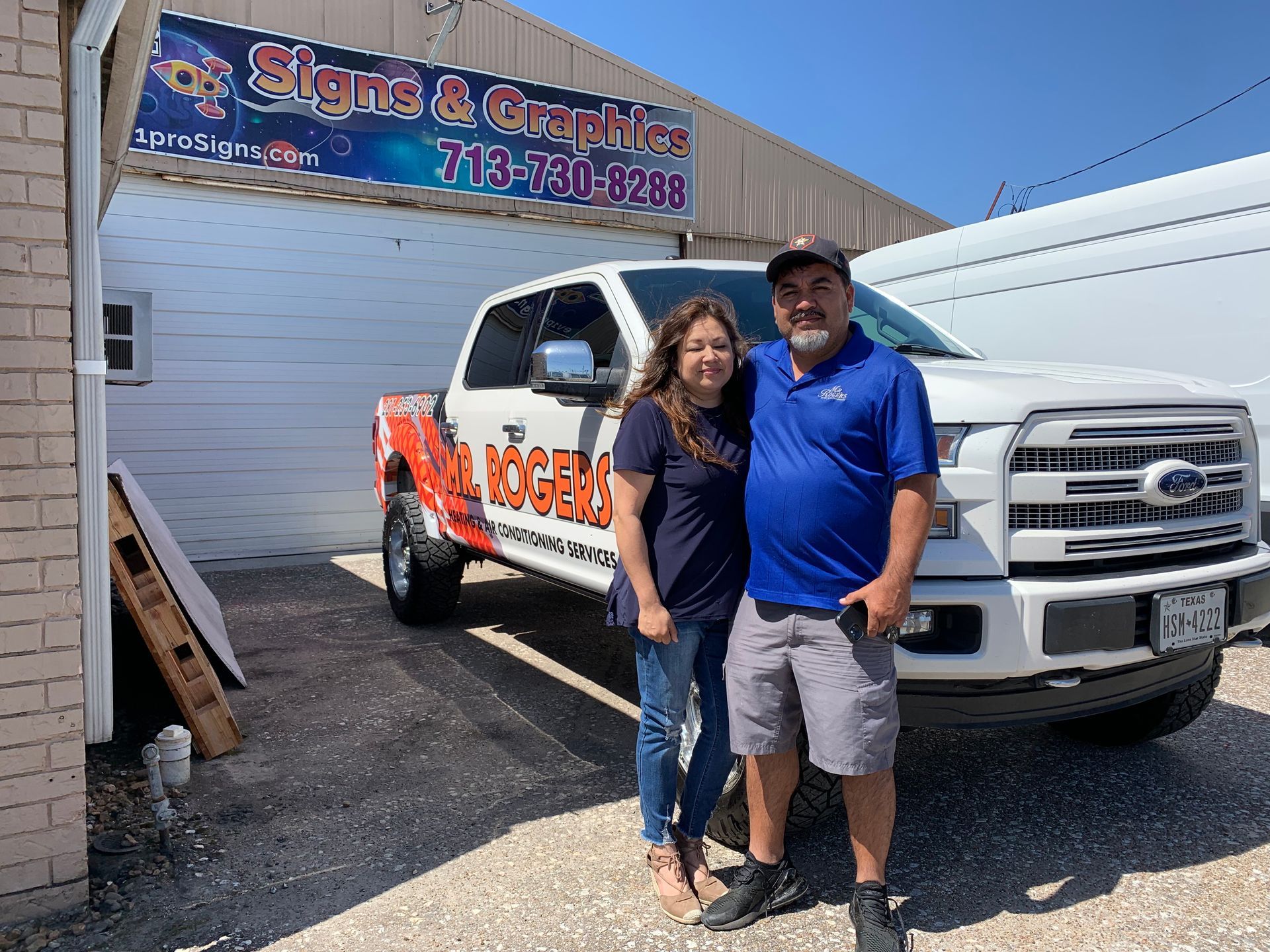 Two people posing in front of a white truck with business signage.