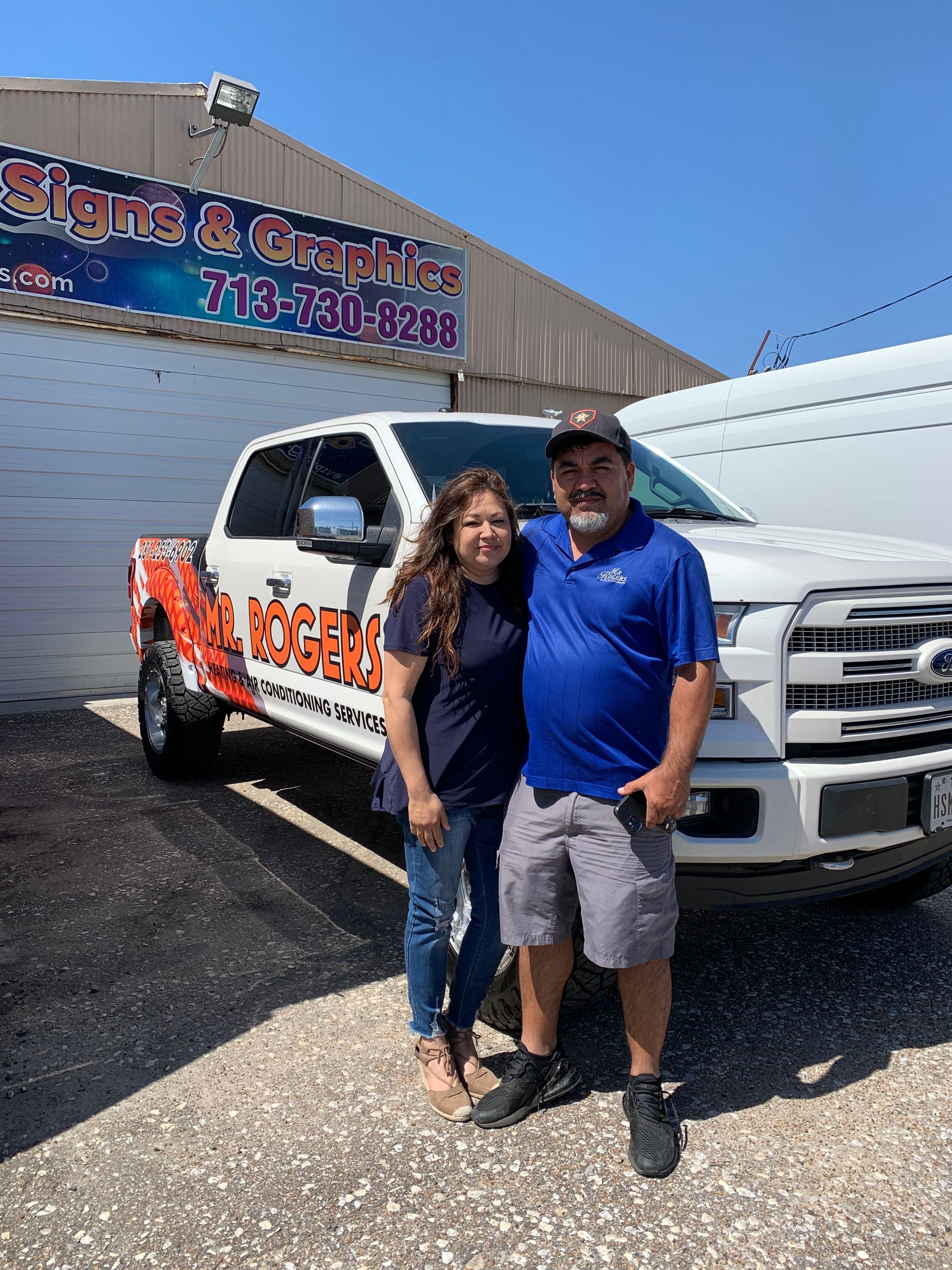 Two people standing next to a white pickup truck with business graphics in front of a building.