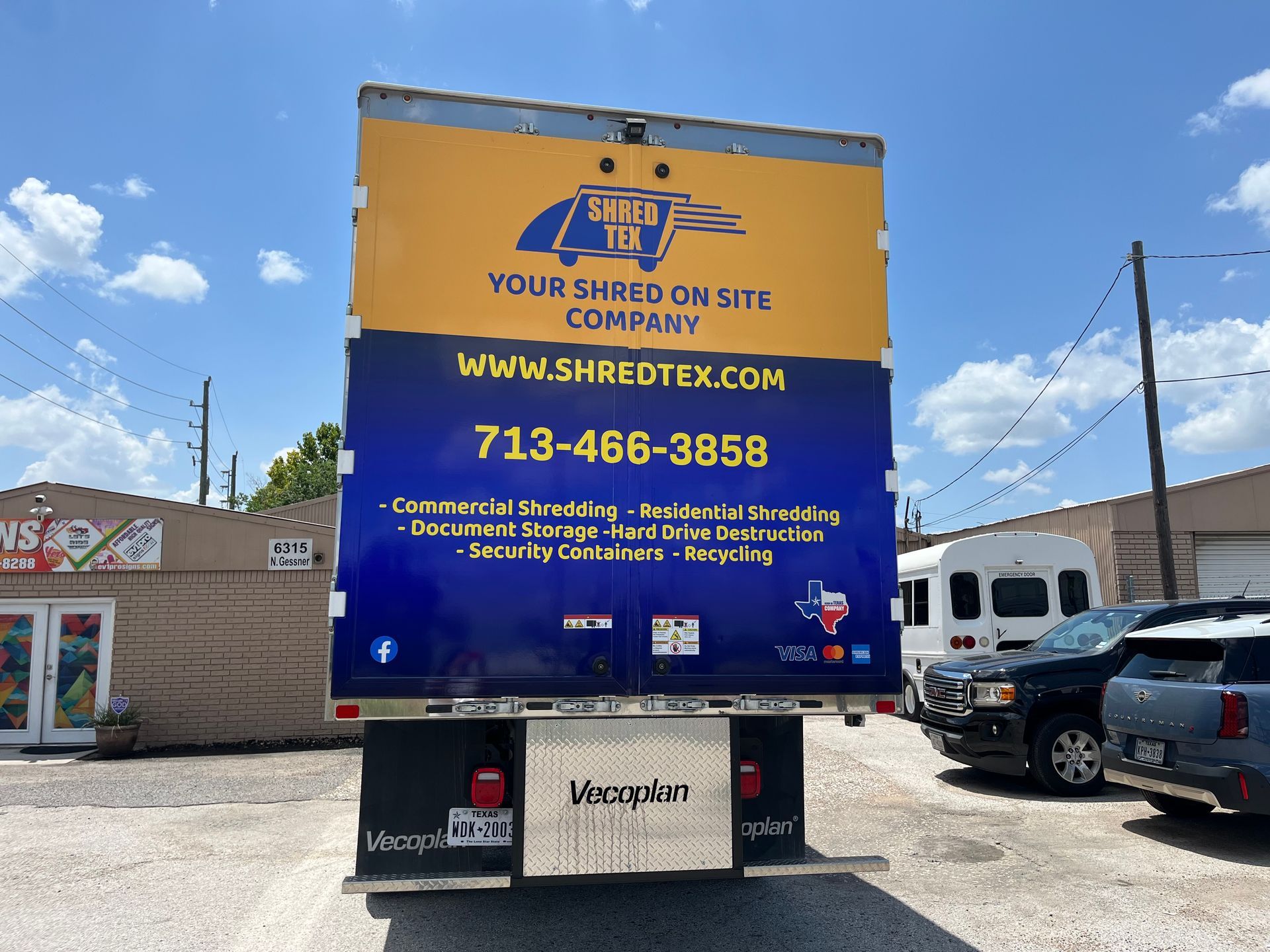 Rear view of a shredding truck. Blue and gold company logo, website address, and phone number on the back of the truck.
