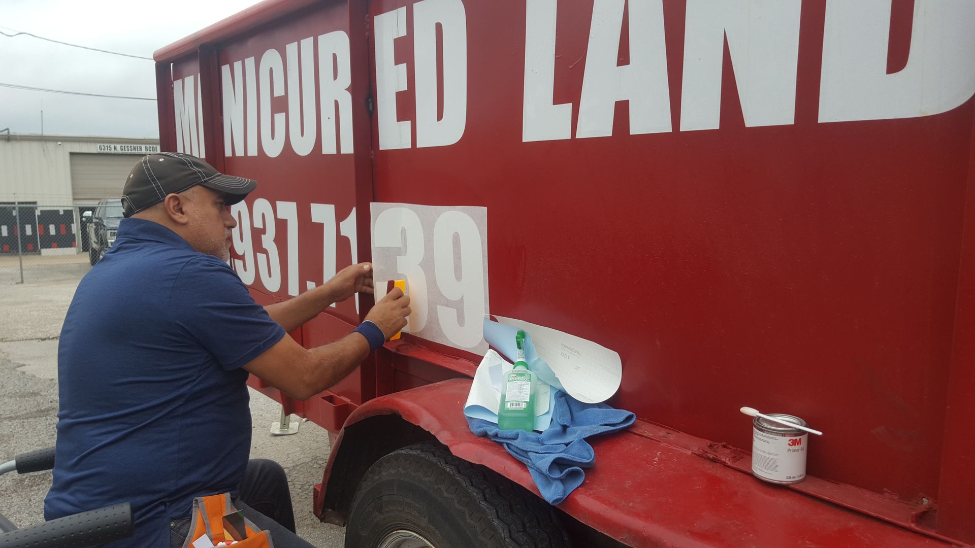 Man applying white numbers to a red dumpster. 
