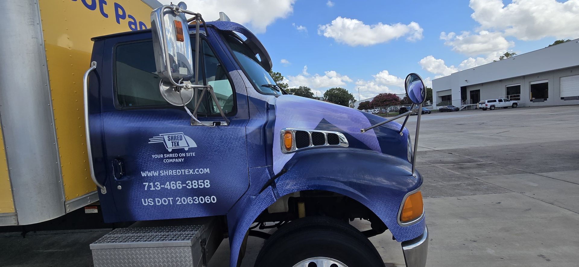 Blue and yellow moving truck parked on a concrete lot on a sunny day with a cloudy sky.