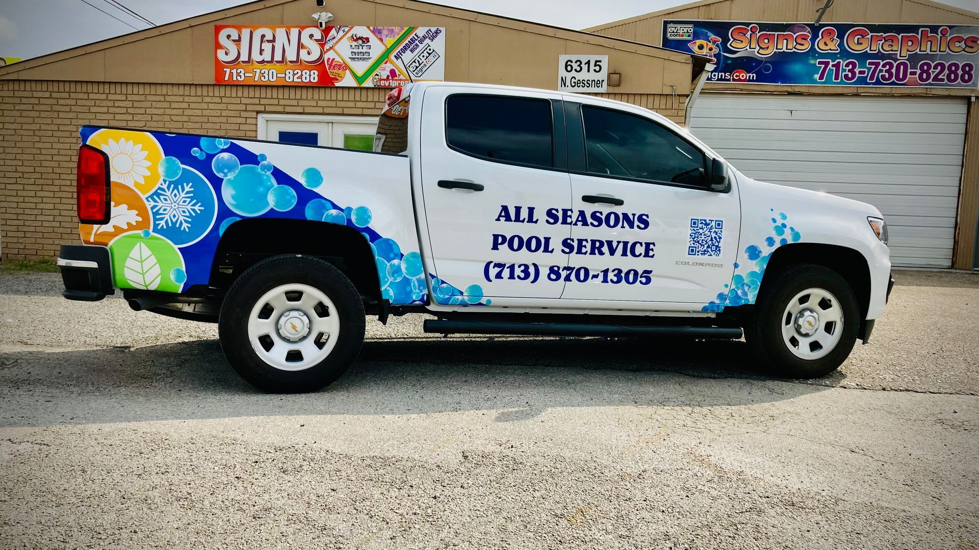 White pickup truck with pool service graphics in front of a sign shop.