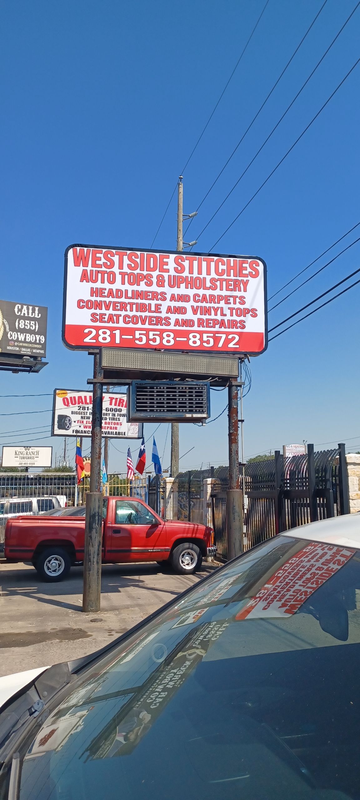 Sign for West Side Stitches Auto Top & Upholstery with red truck parked in front.