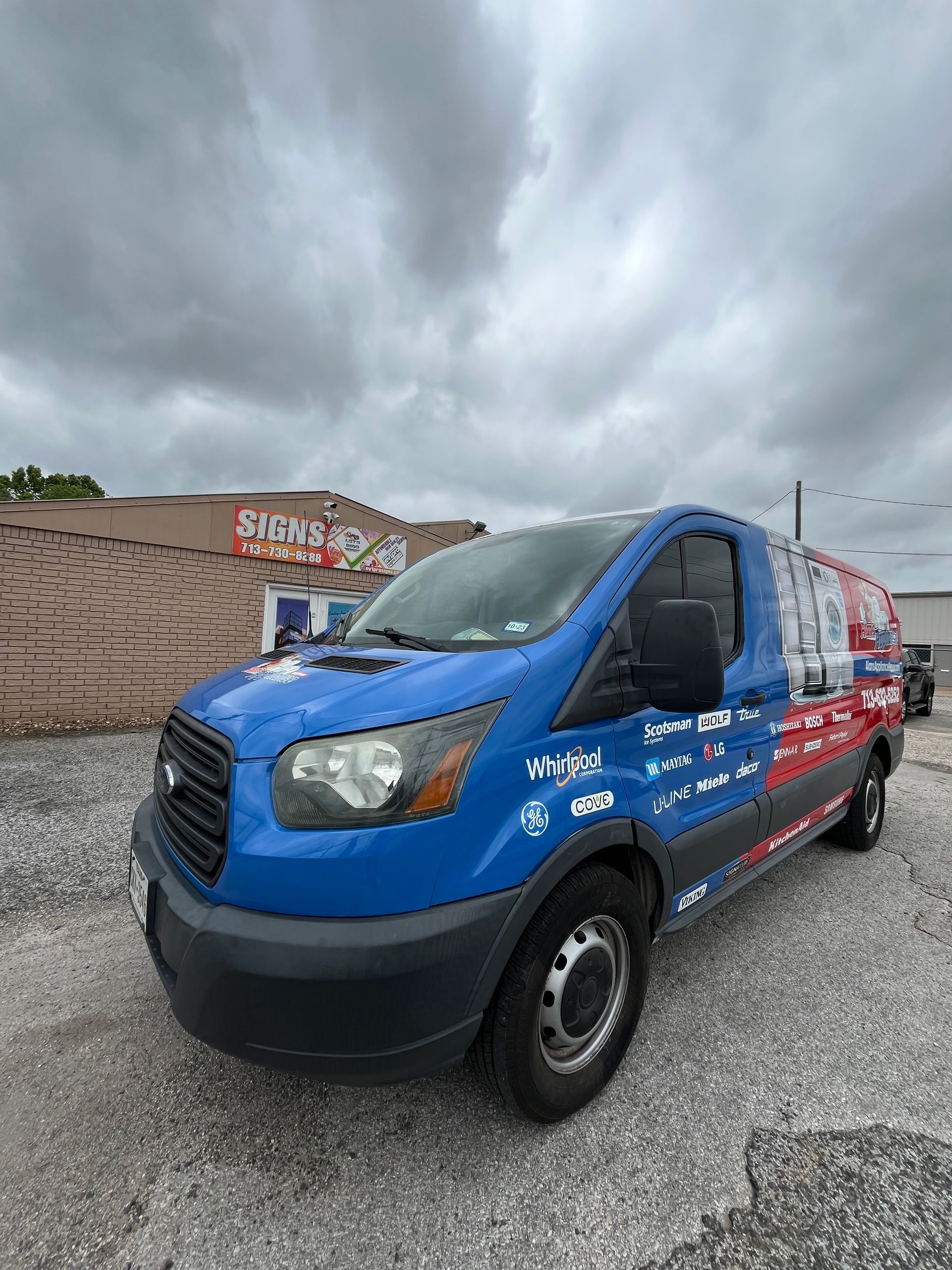 Blue and red van with business logo parked outside a building with a cloudy sky.