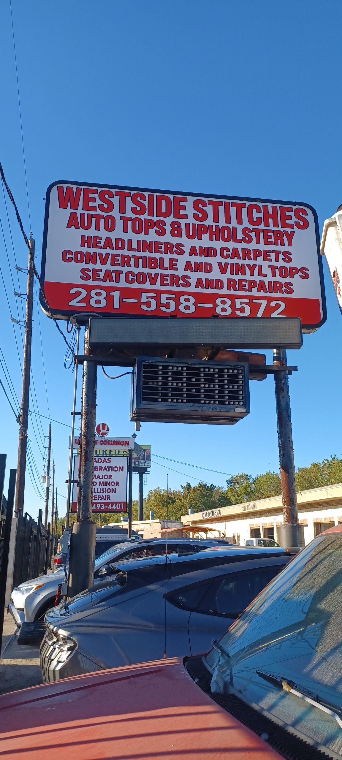 Sign for Westside Stitches, auto upholstery shop, with contact info. Cars parked in front of the shop. Blue sky.