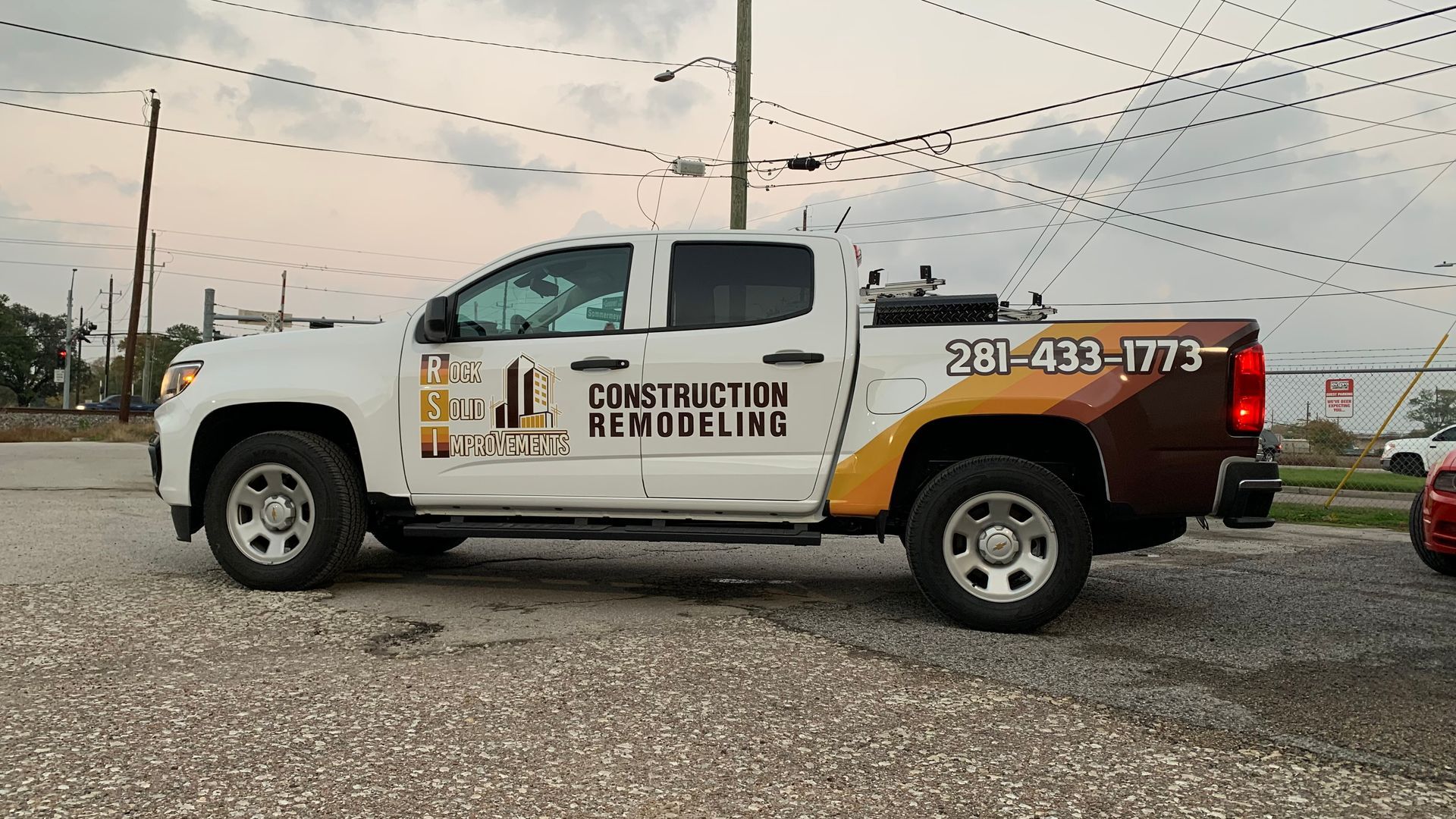 White pickup truck with construction company logo parked on a gravel lot under power lines.