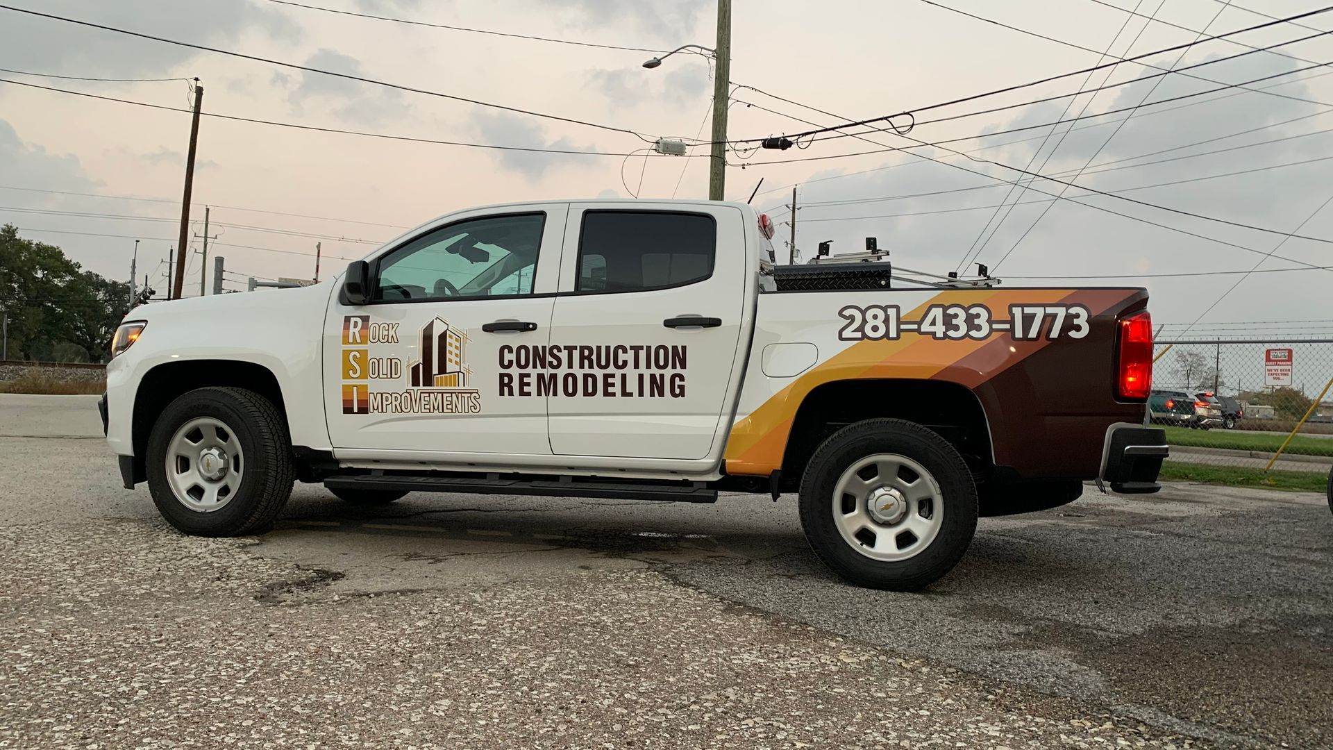 White construction truck with company logo and phone number parked on a paved lot.