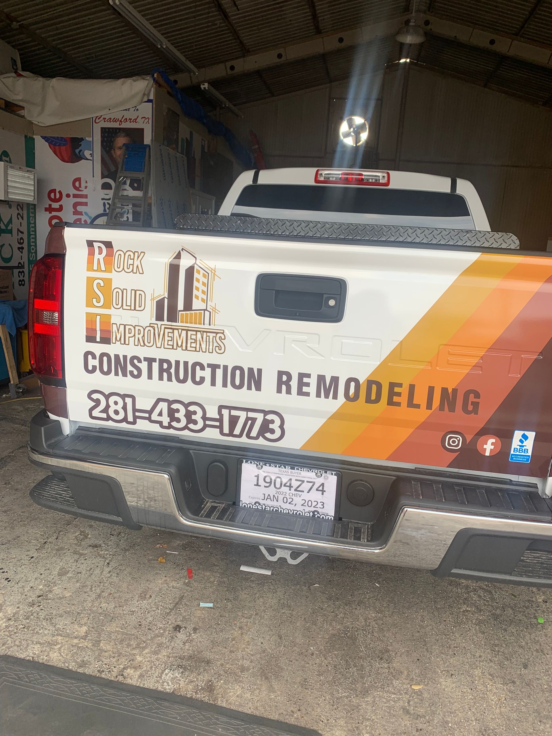 Rear view of a pickup truck with construction company branding and phone number.