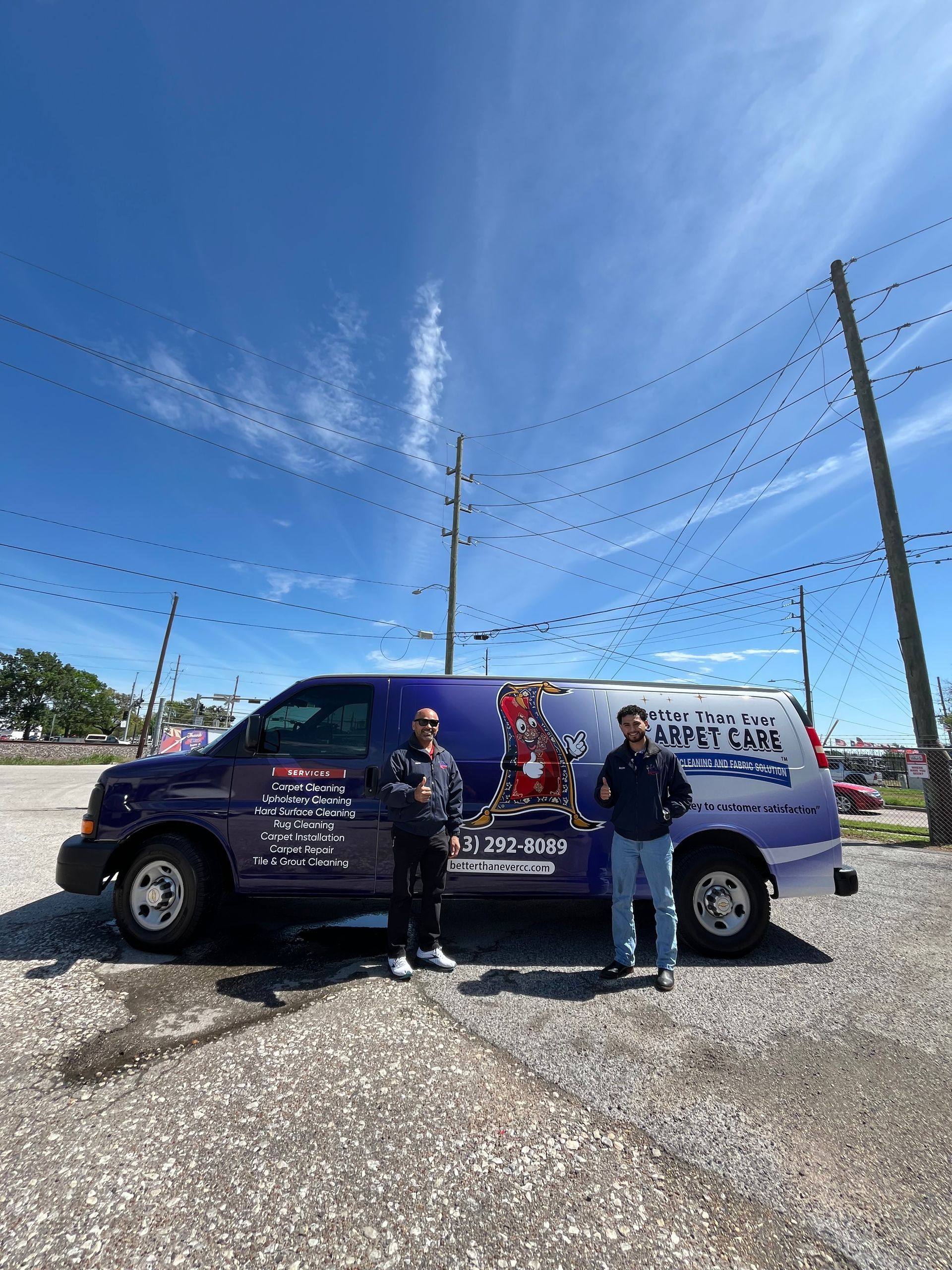 Two men stand beside a branded purple van against a blue sky, outdoors.