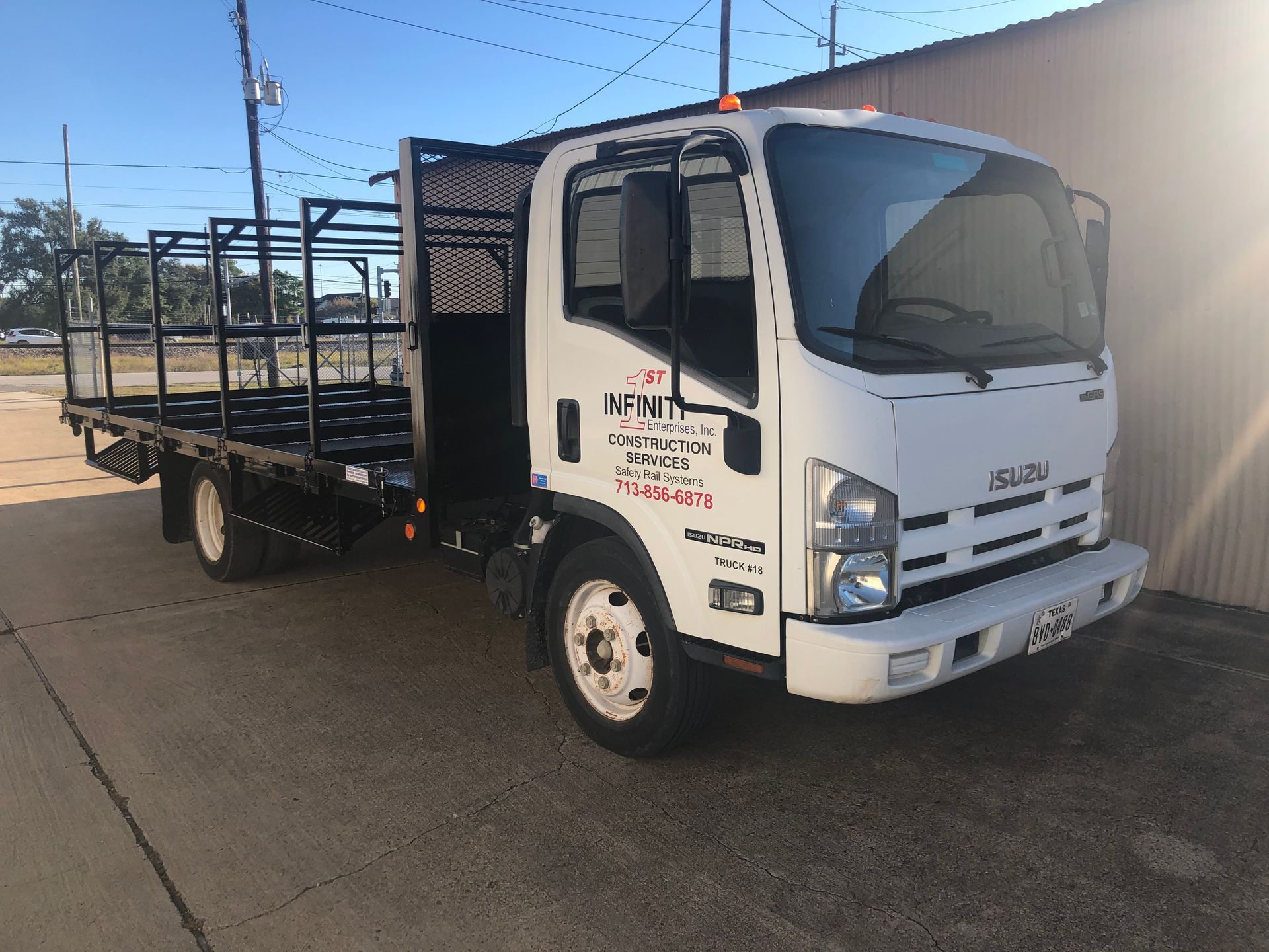 White Isuzu flatbed truck with black metal sides parked on pavement.