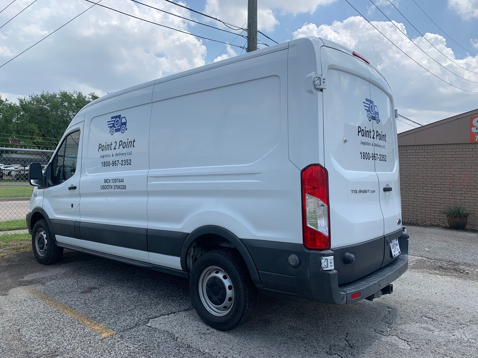White van with company logos parked on a street. Cloudy sky in the background.